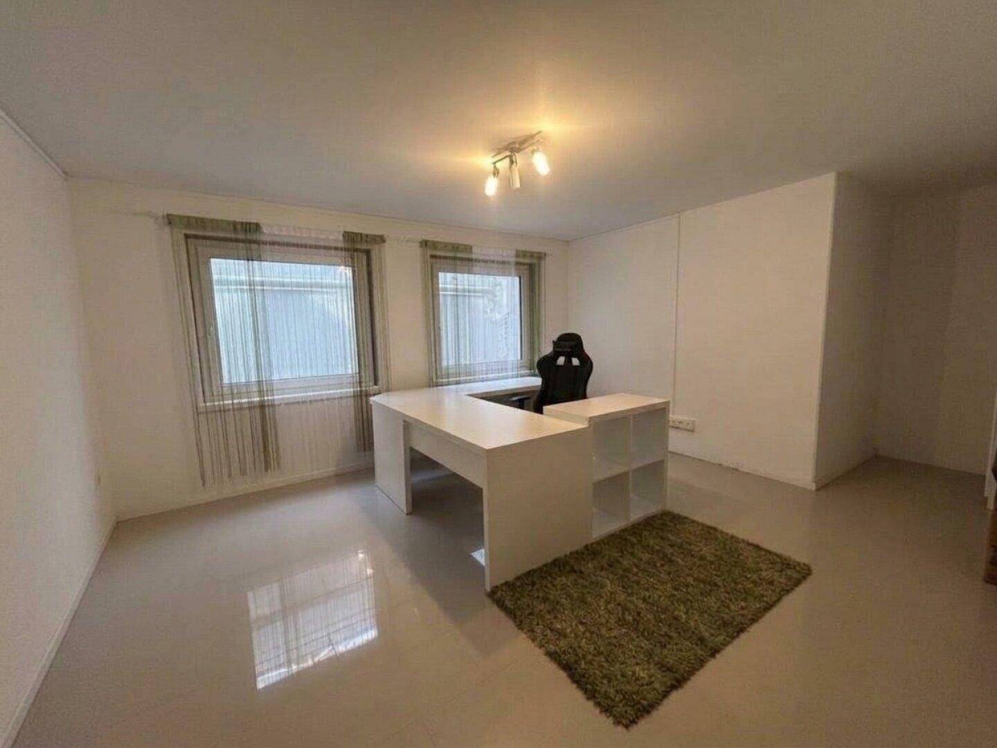 Helles Arbeitszimmer mit modernem Schreibtisch, Teppich und zwei Fenstern für viel Tageslicht.