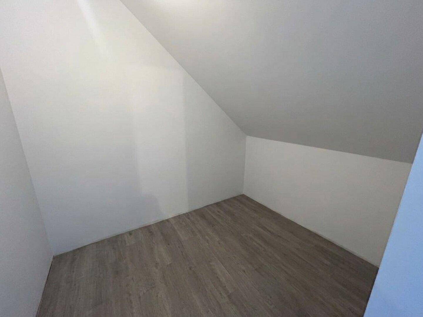 Leerer Abstellraum im Dachgeschoss mit schrägen Wänden und Laminatboden für zusätzlichen Stauraum.