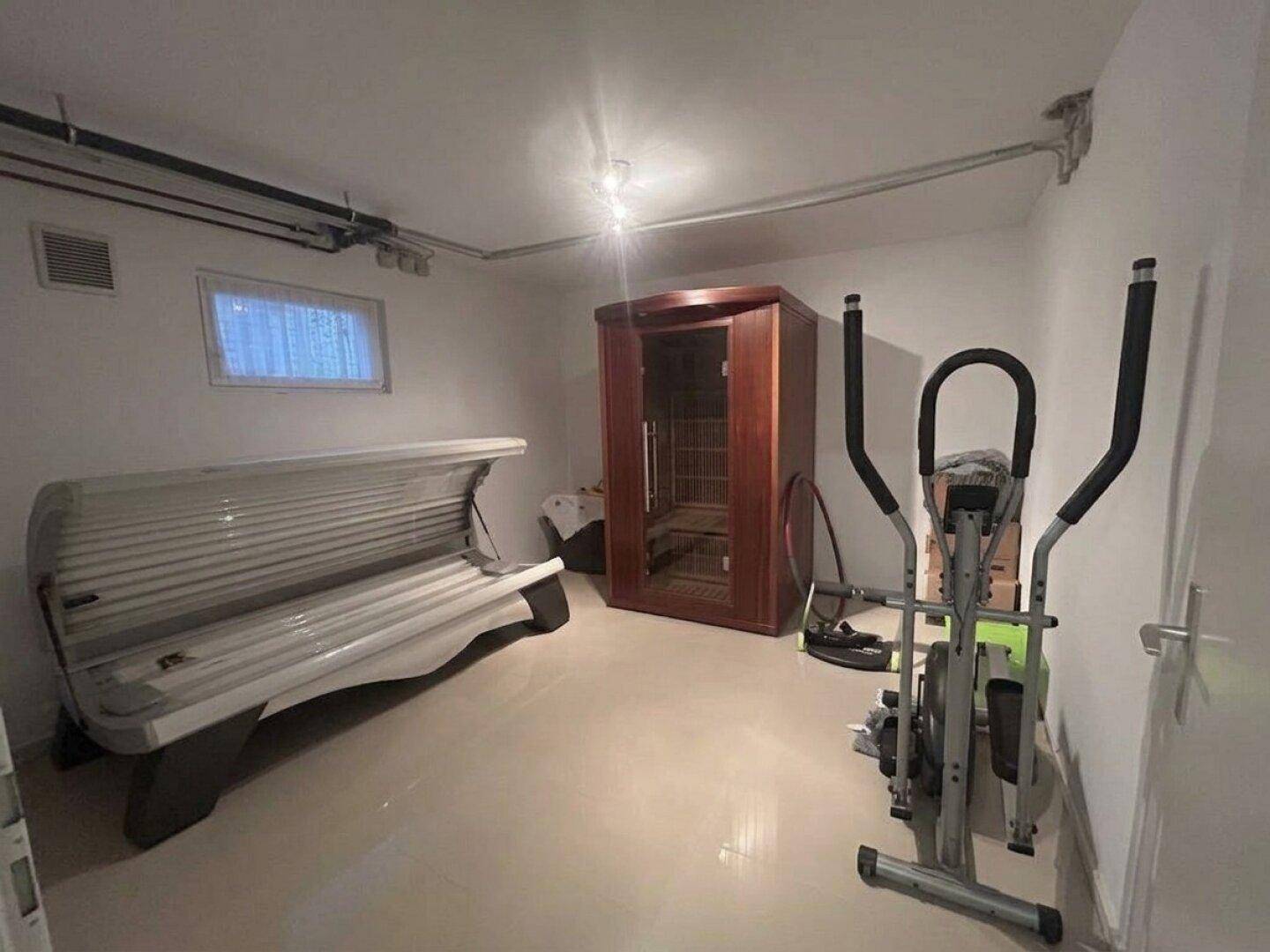 Fitnessraum im Keller mit Solarium, Trainingsgerät und einer Infrarot-Saunakabine für Wellness.
