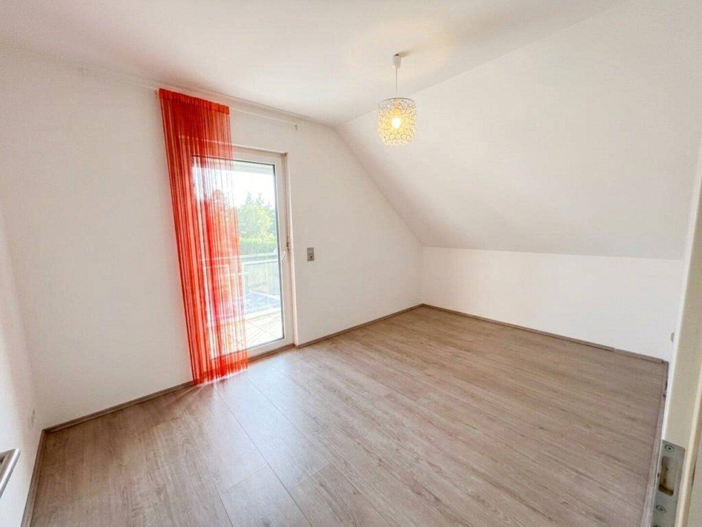 Helles Schlafzimmer im Dachgeschoss mit Laminatboden und Zugang zu einem kleinen Balkon.