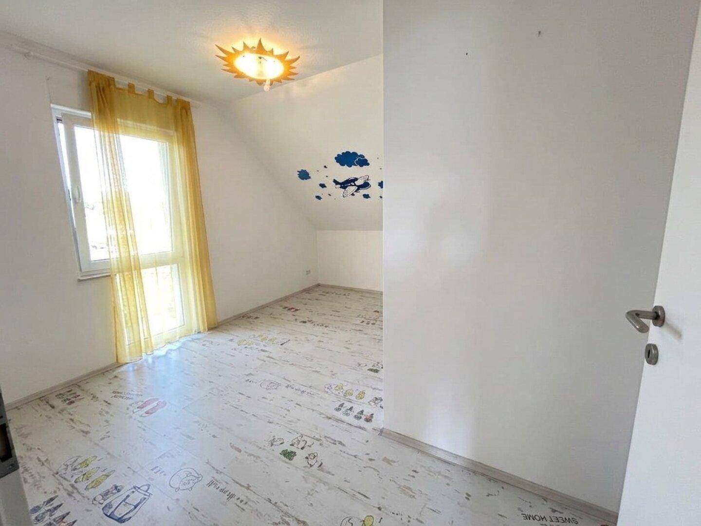 Helles Kinderzimmer mit spielerischem Laminatboden, großem Fenster und schrägen Wänden.