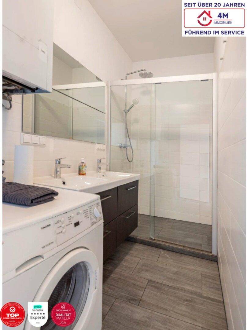 Modernes Badezimmer mit Doppelwaschbecken, großer Duschkabine und integrierter Waschmaschine.