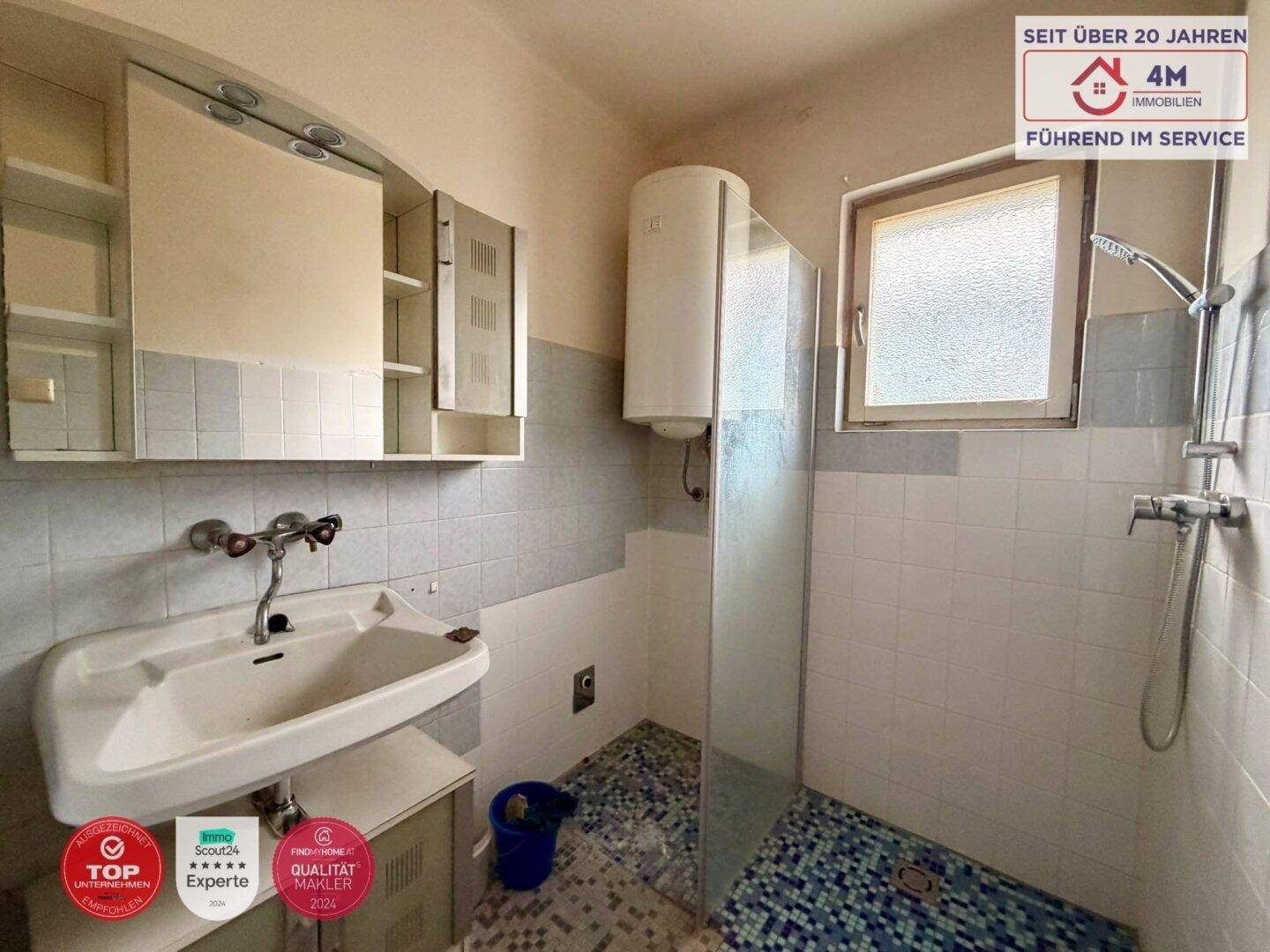 Badezimmer mit Dusche, Waschbecken, Boiler und Fenster für natürliche Belüftung.