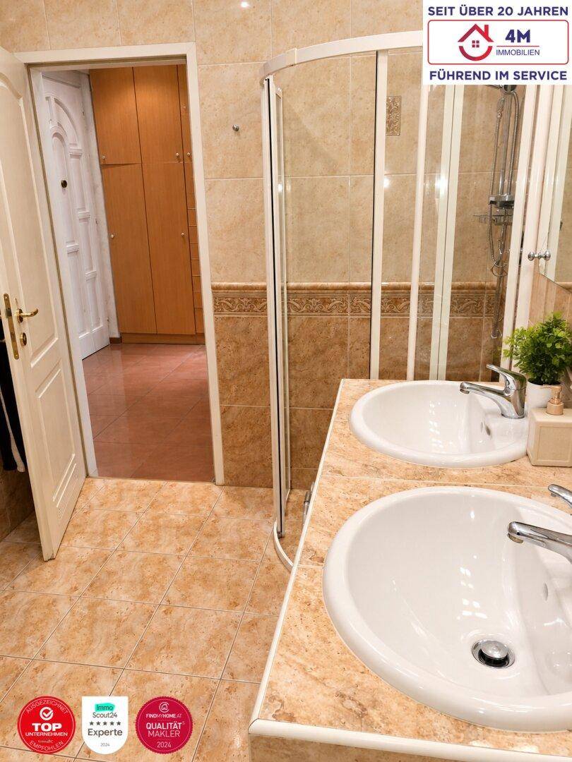 Badezimmer mit doppelten Waschbecken, Duschkabine und beigefarbenen Fliesen.