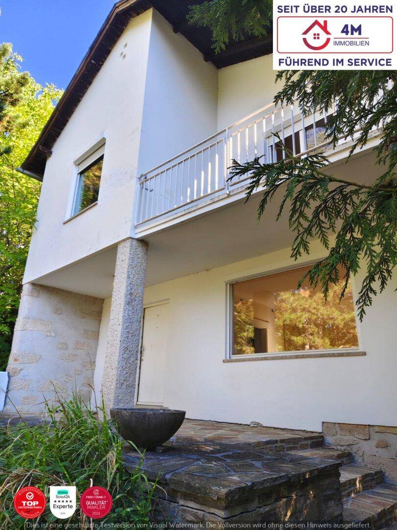 Die Hausfassade zeigt einen Balkon mit Geländer und eine Steintreppe zum Eingangsbereich.