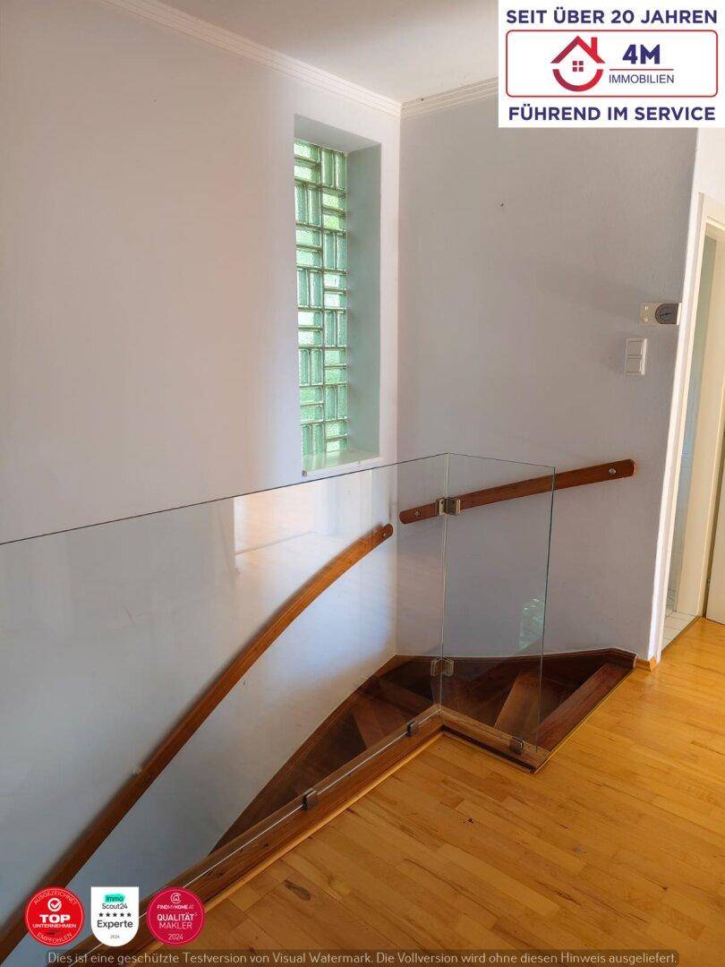 Treppenhaus mit Holzstufen, Glasgeländer und einem Fenster aus Glasbausteinen.