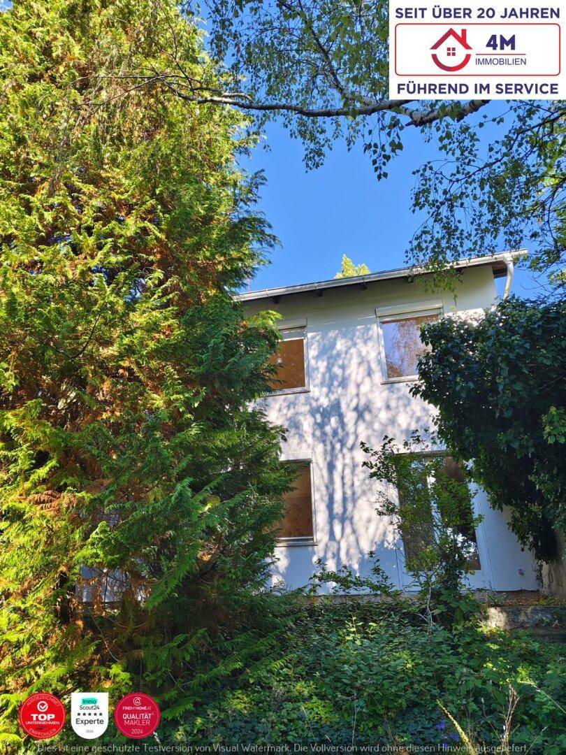 Das Wohnhaus ist teilweise von dichtem Grün verdeckt und zeigt eine helle Fassade.