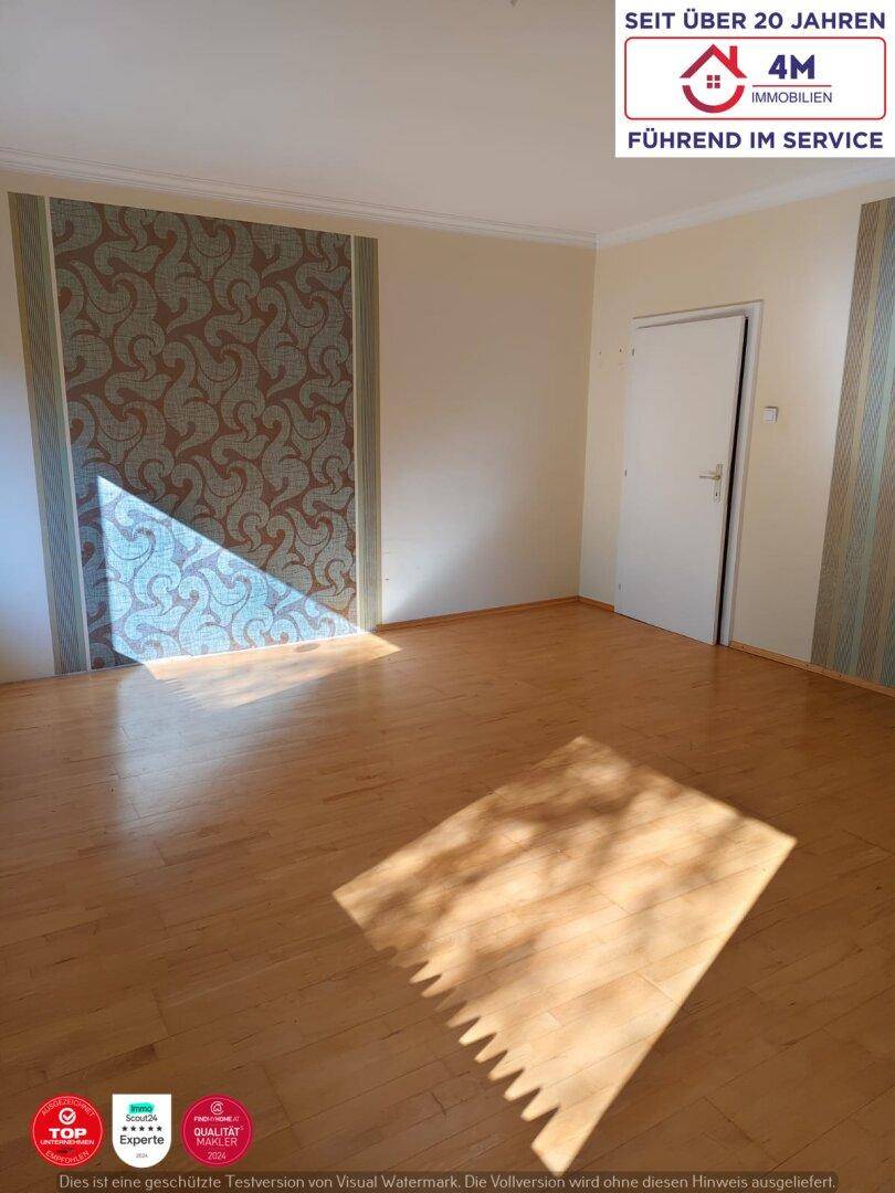 Helles Wohnzimmer mit Parkettboden und dekorativer Tapete, durchflutet von natürlichem Licht.