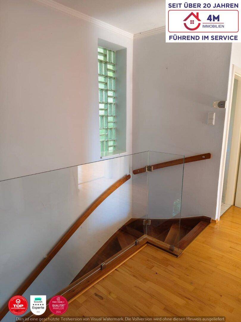 Treppenhaus mit Holzstufen, Glasgeländer und einem Fenster aus Glasbausteinen.