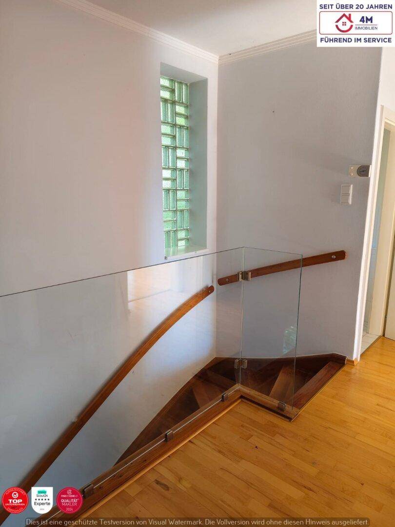 Treppenhaus mit Holzstufen, Glasgeländer und einem Fenster aus Glasbausteinen.