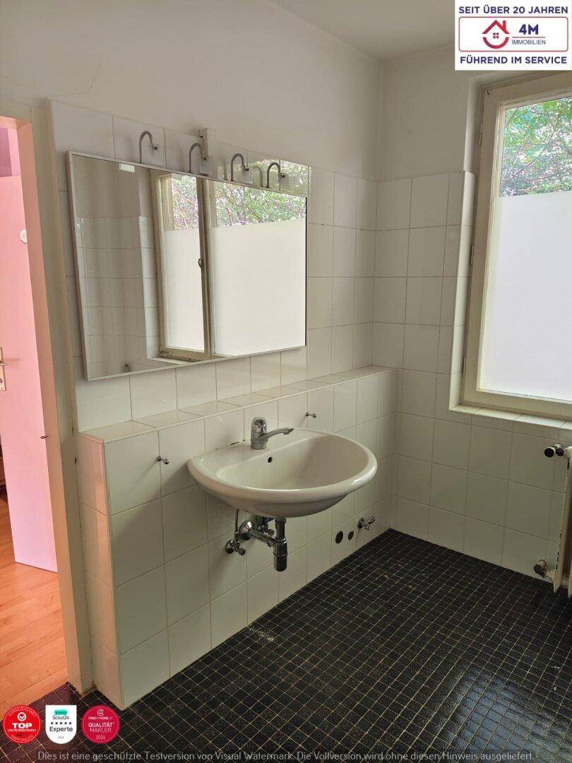 Badezimmer mit Waschbecken, Spiegel, weißen Wandfliesen und dunklem Boden.
