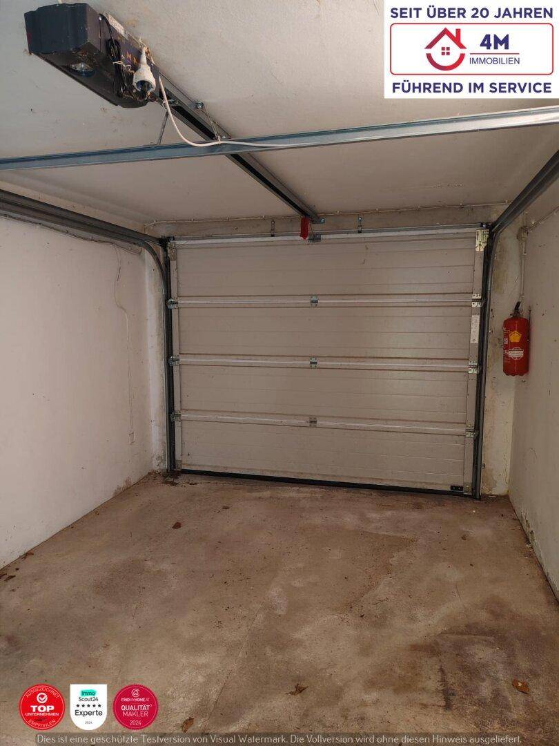 Eine Garage mit Sektionaltor und Betonboden, ausgestattet mit einem Feuerlöscher.