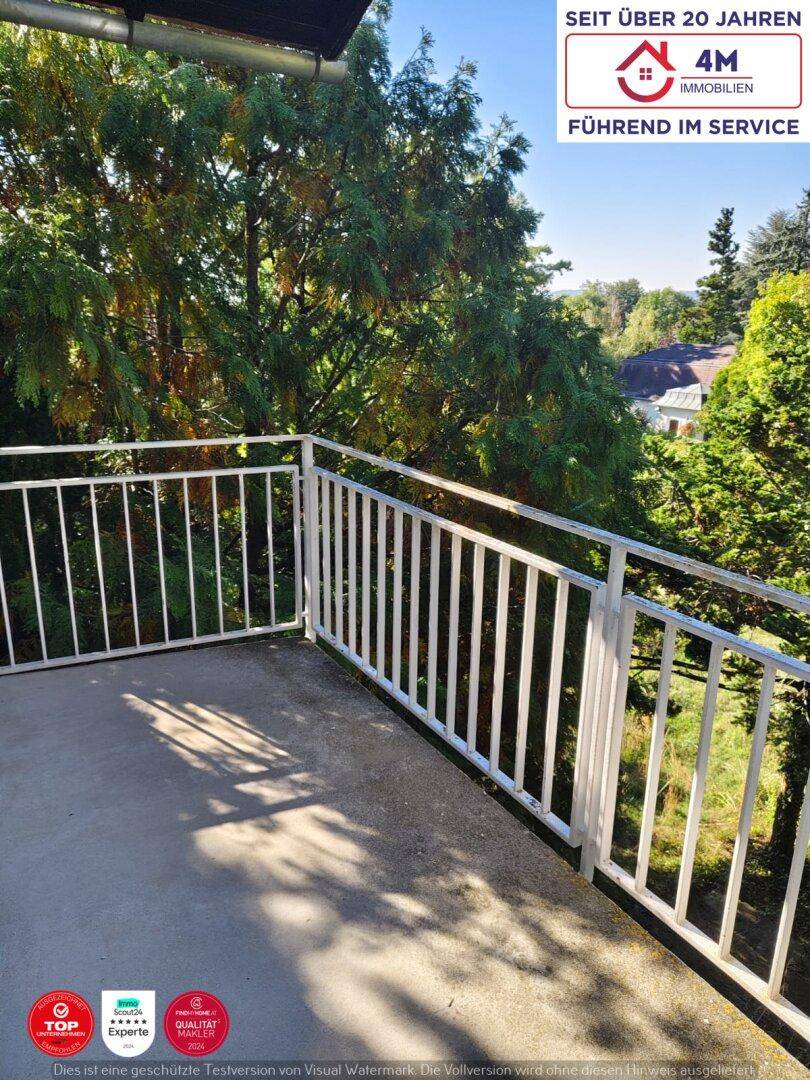 Sonniger Balkon mit weißem Geländer und Ausblick auf Bäume und Häuser.