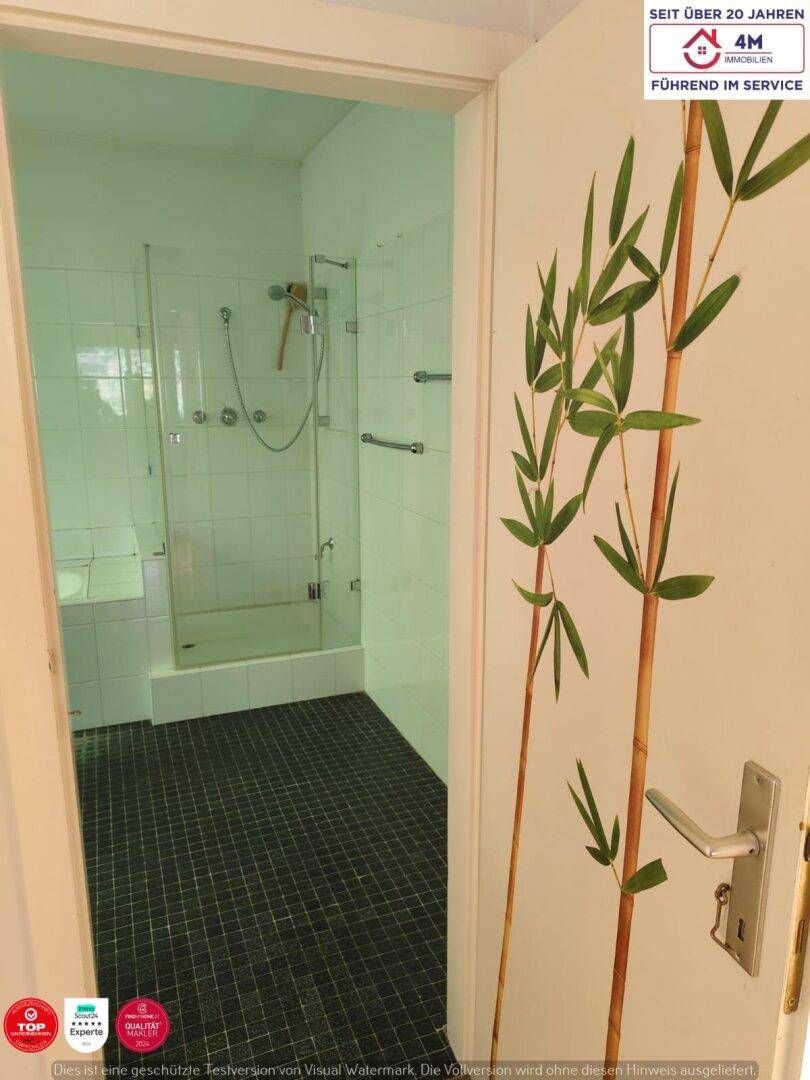 Badezimmer mit Duschkabine und weißen Fliesen, durch eine Tür mit Bambusmotiv zugänglich.