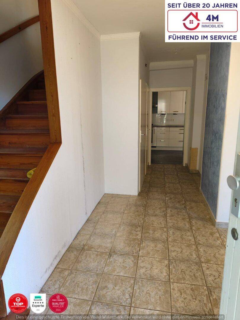Flur mit Fliesenboden und Holztreppe, der in den Küchenbereich führt.