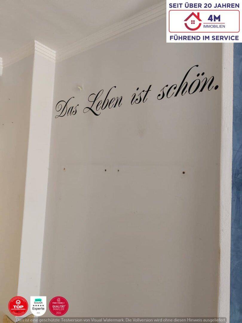 Eine weiße Wand mit der Aufschrift "Das Leben ist schön" und Stuckverzierung an der Decke.