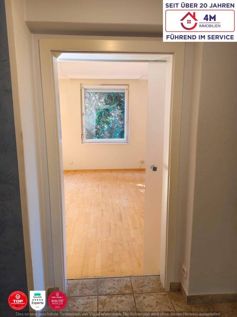 Ein heller Raum mit Parkettboden und einem großen Fenster, das viel Tageslicht hereinlässt.