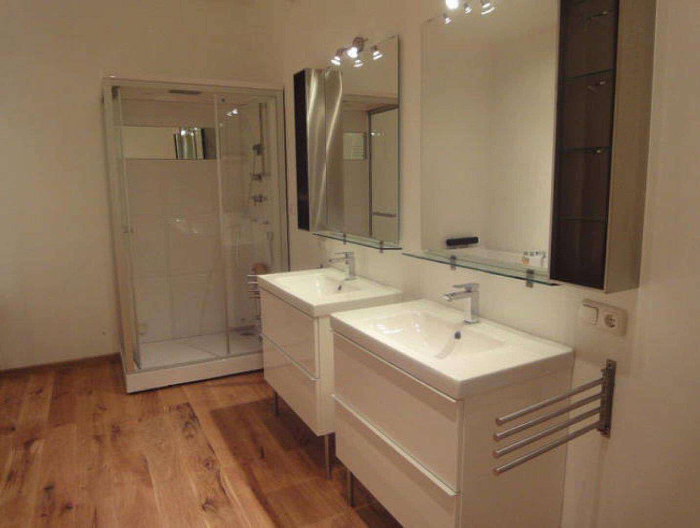 Modernes Badezimmer mit Doppelwaschbecken, einer Duschkabine und warmem Holzboden.