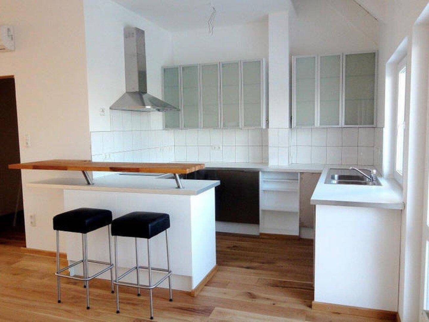 Moderne Einbauküche mit Dunstabzugshaube, weißen Schränken und einer praktischen Frühstücksbar.