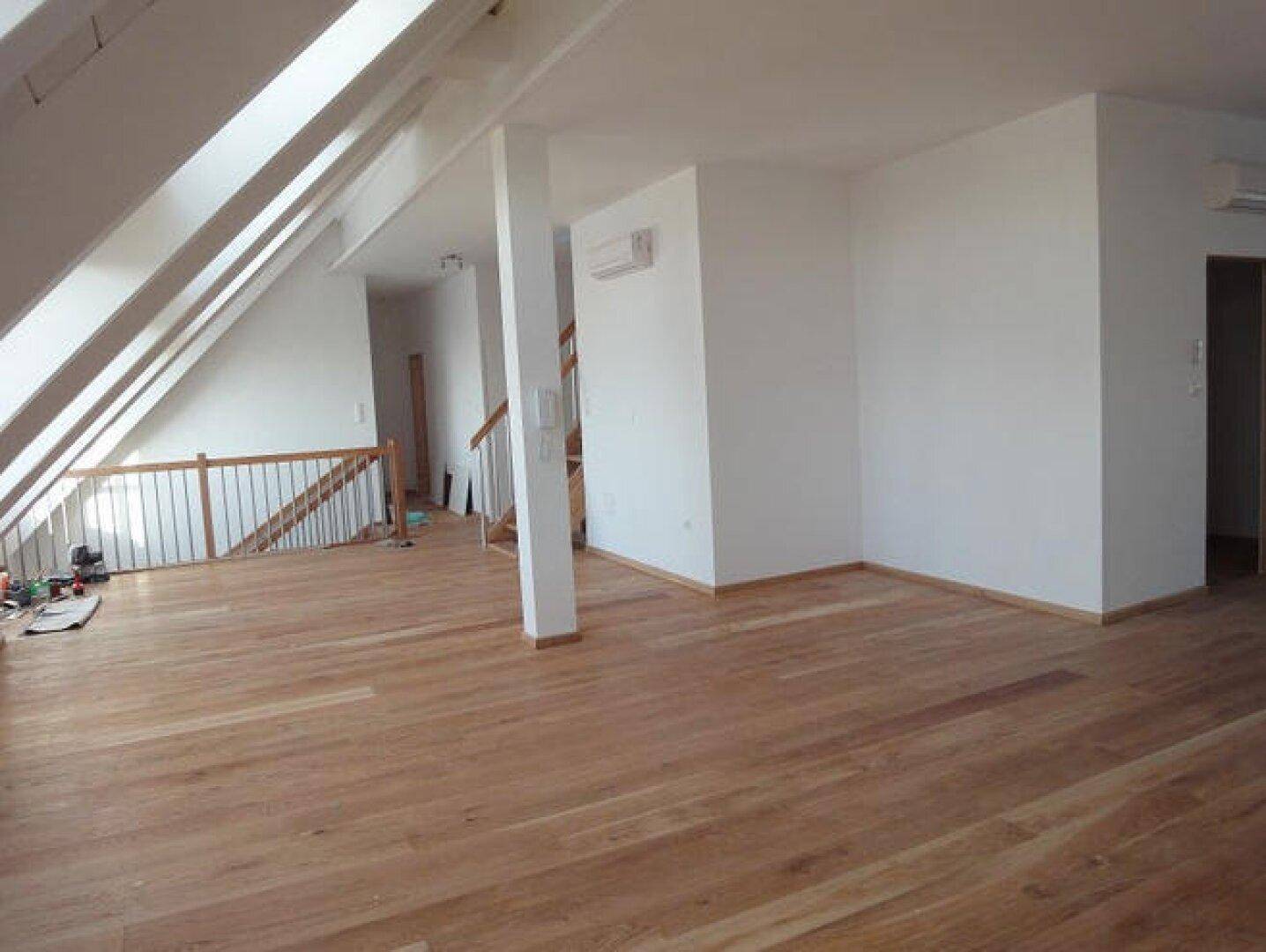 Geräumiger Dachbodenraum mit Holzboden, schrägen Decken und viel Tageslicht durch die Dachfenster.
