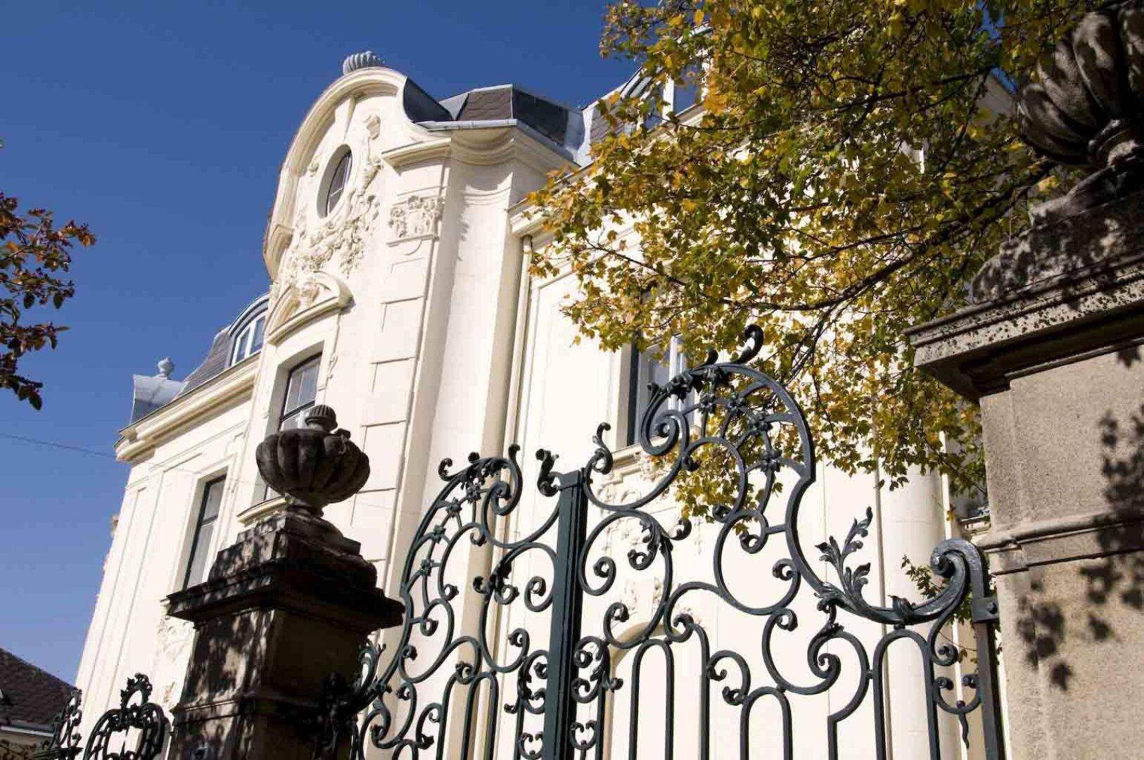 Elegante Fassade eines historischen Gebäudes mit kunstvollem schmiedeeisernem Tor und üppiger Verzierung.