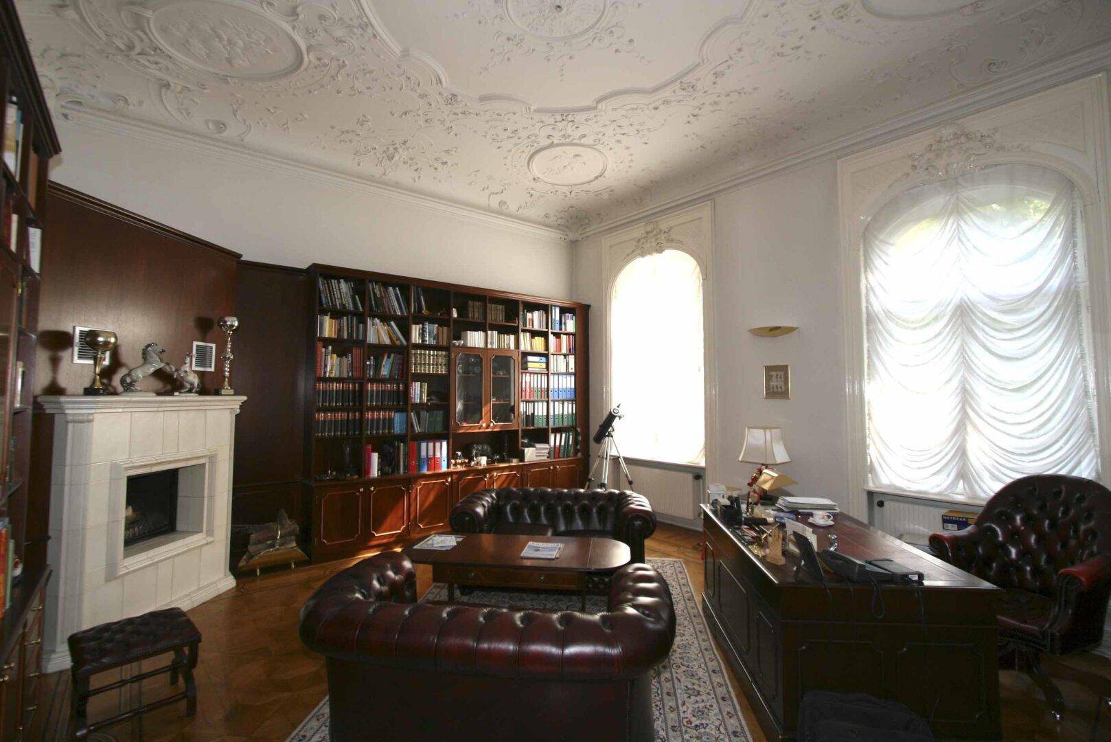 Stilvolles Arbeitszimmer mit Ledersofas, Kamin, Bücherregalen und großen Fenstern.