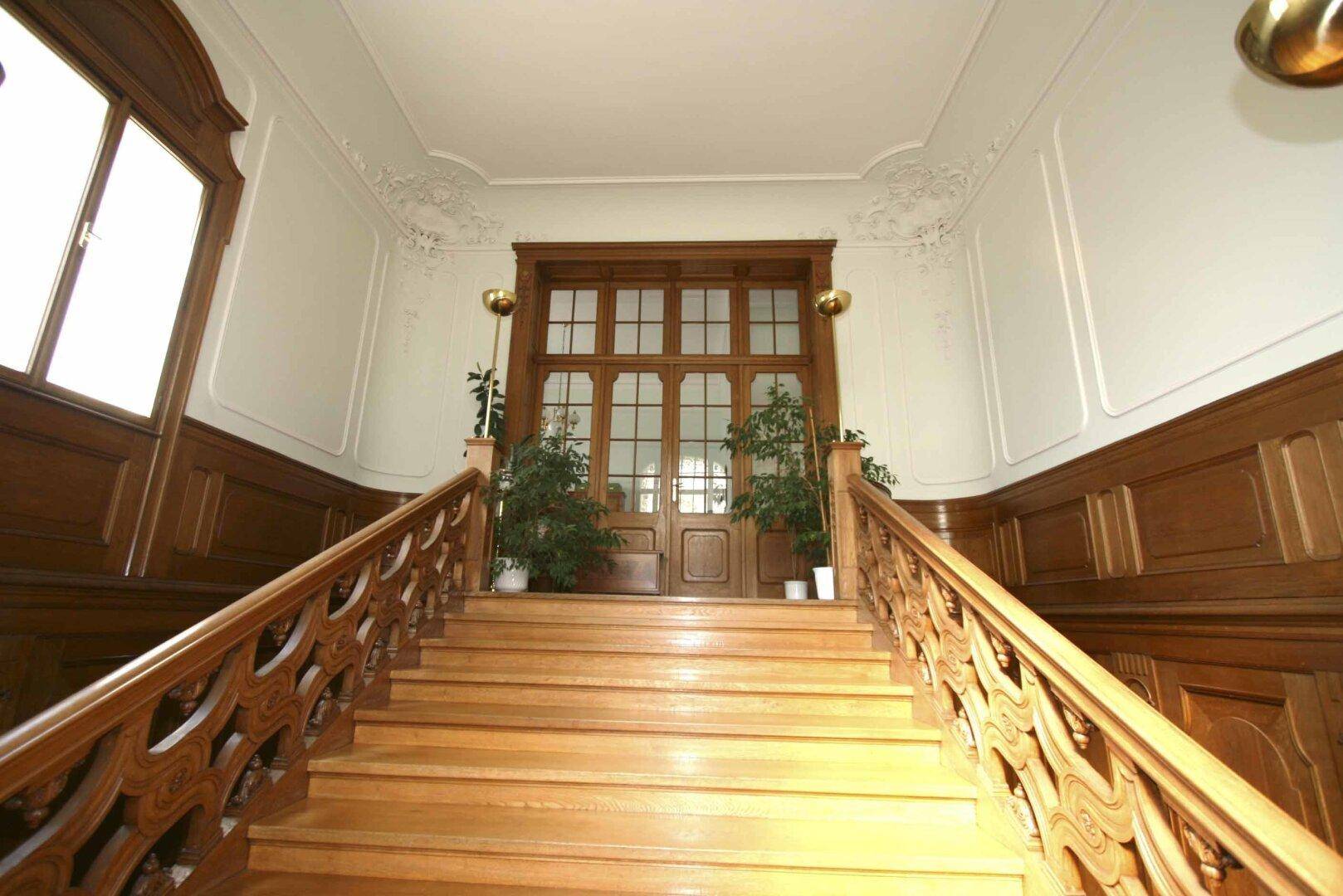 Eindrucksvolles Treppenhaus mit kunstvoll geschnitztem Holzgeländer und hohen Decken.