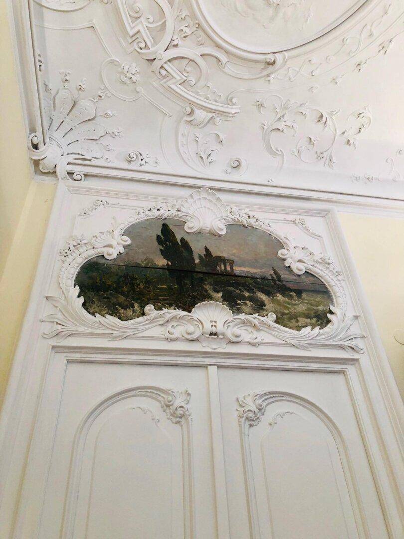 Detail einer kunstvoll verzierten Tür mit Übermalung und aufwendiger Stuckdecke.