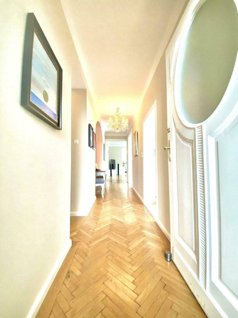 Langer, heller Flur mit Fischgrätparkett und einem Gemälde an der Wand, der zu weiteren Räumen führt.
