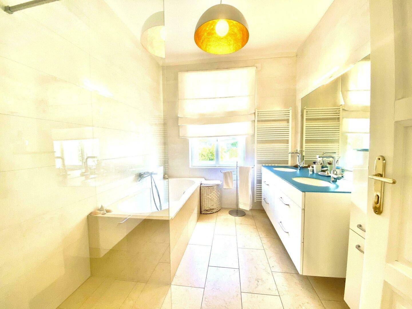 Helles Badezimmer mit Badewanne, Doppelwaschbecken und einem Fenster für natürliche Belüftung.