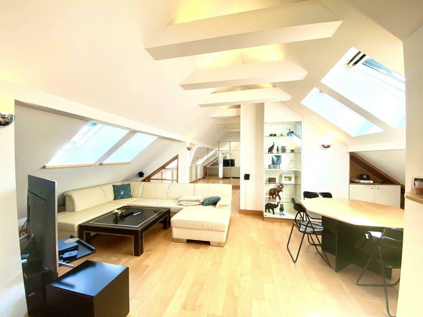 Heller Wohn- und Essbereich im Dachgeschoss mit mehreren Dachfenstern und modernem Interieur.