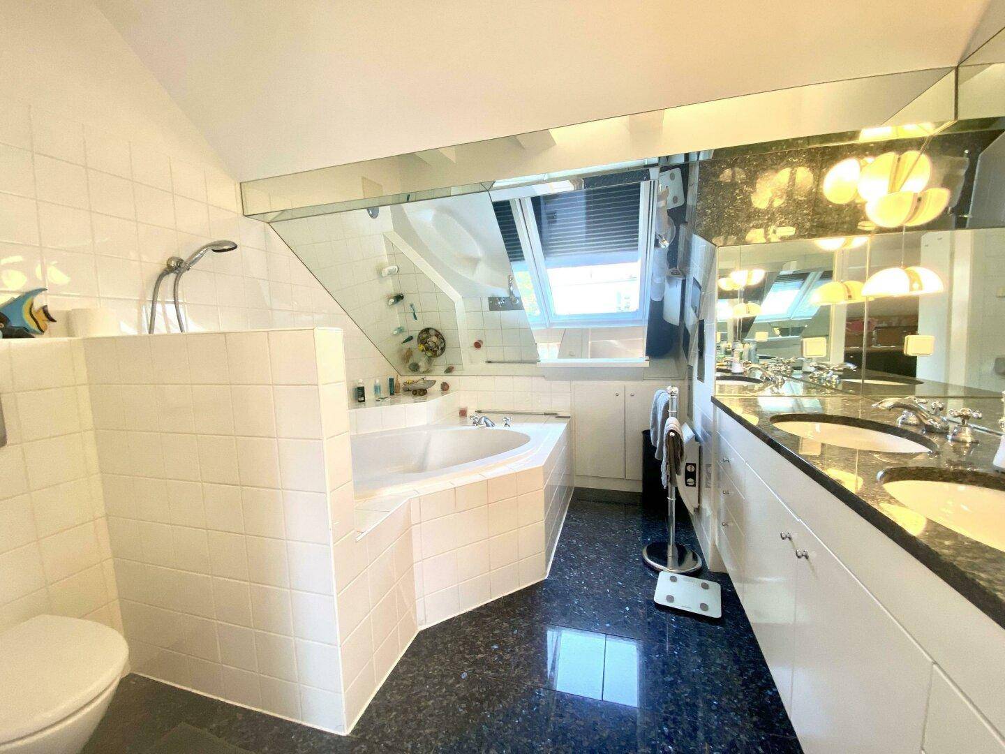 Dachgeschoss-Badezimmer mit Eckbadewanne, Doppelwaschbecken und dunklem Granitboden unter Schrägdach.