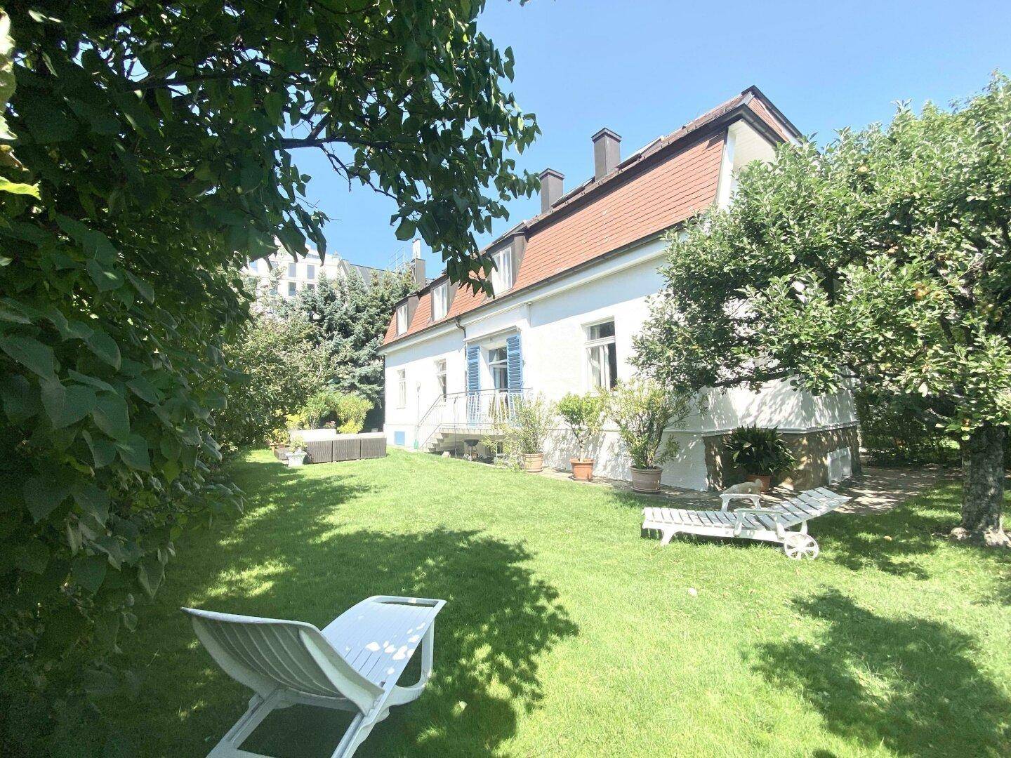Großer, gepflegter Garten mit Rasenfläche und Blick auf die Hausfassade mit blauen Fensterläden.