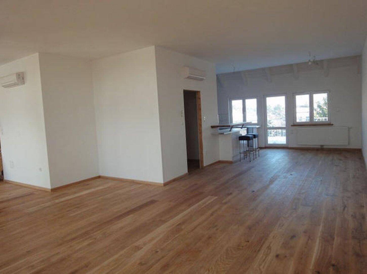 Heller, offener Raum mit Holzboden, großen Fenstern und einer Bar, ideal für Wohn- und Essbereich.