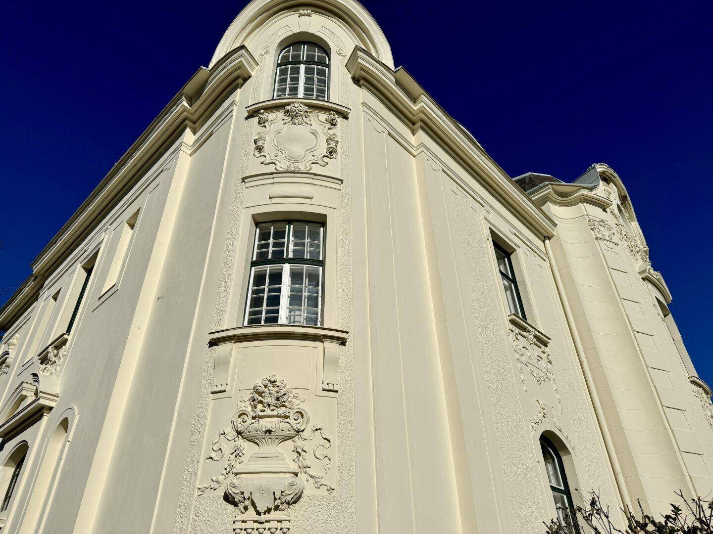 Detailansicht der historischen Fassade mit reich verzierten Elementen und Rundbogenfenstern unter blauem Himmel.