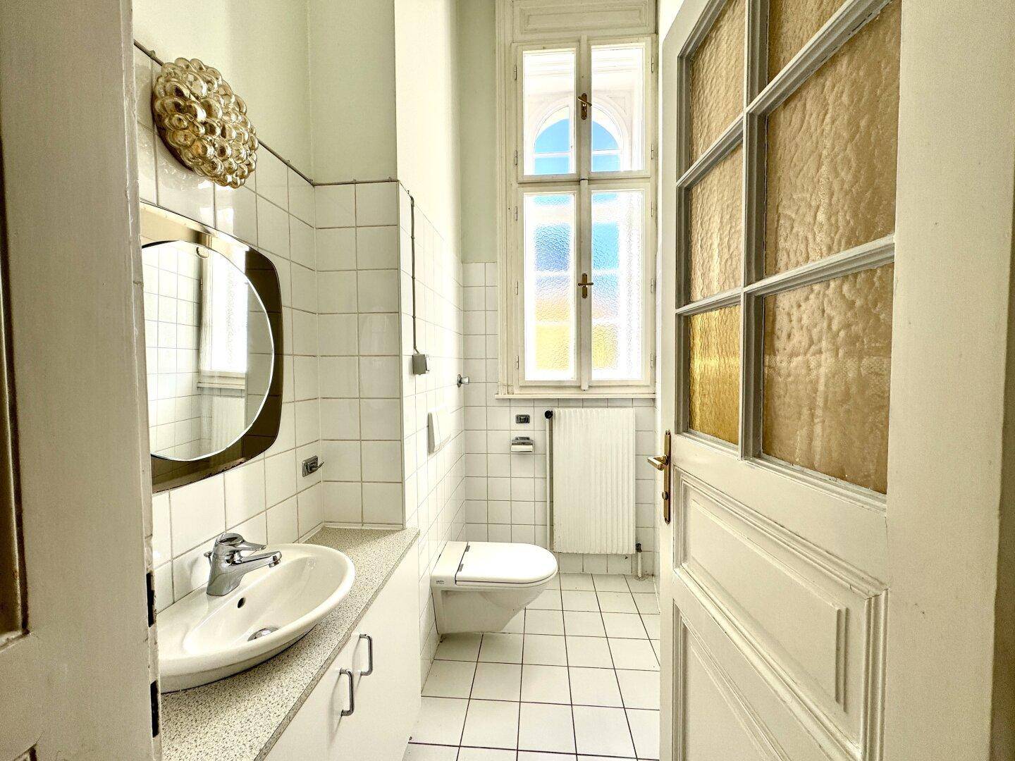 Kleines Badezimmer mit WC, Waschbecken und Fenster, hell gefliest und funktional eingerichtet.