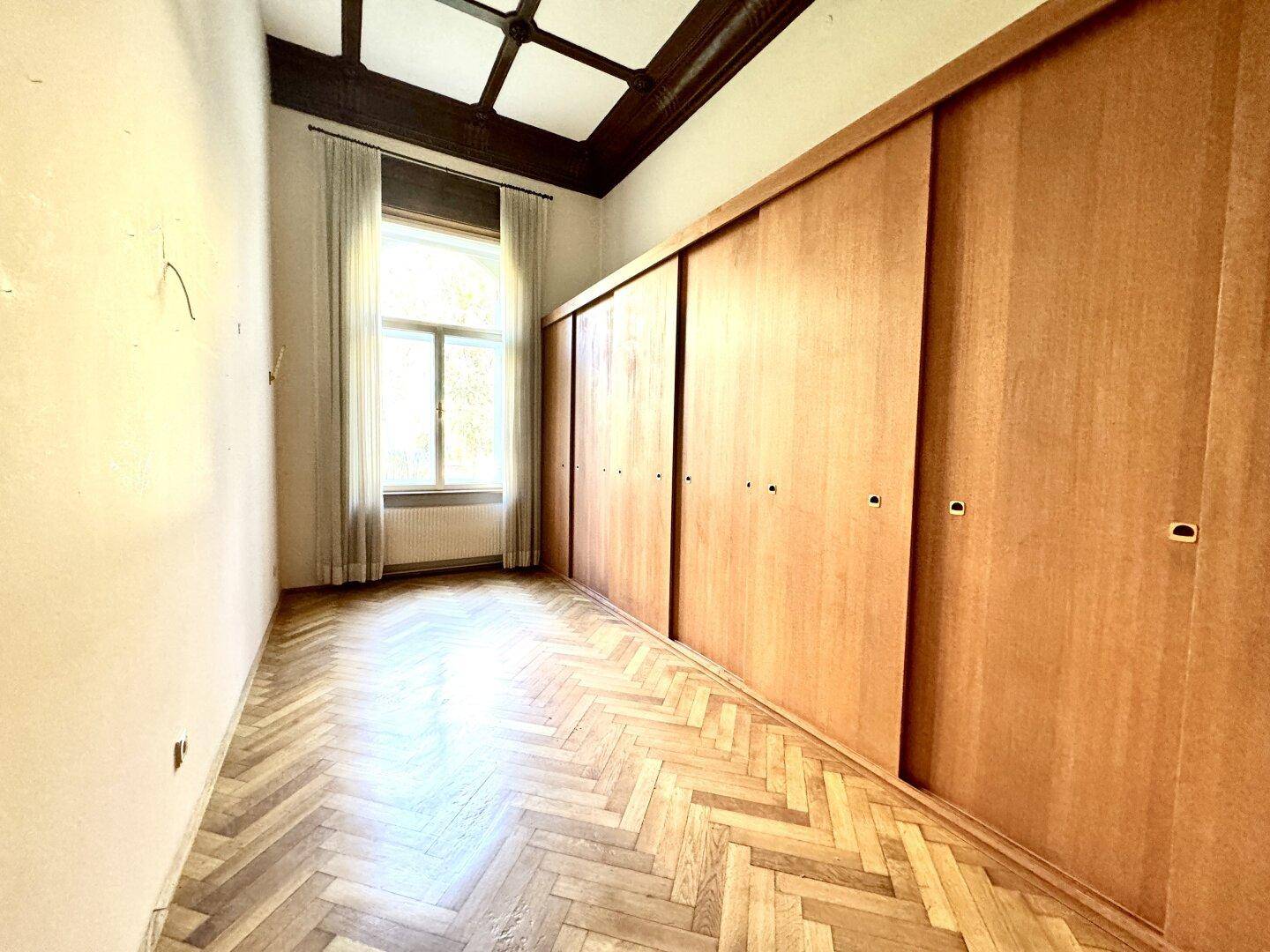 Schlafzimmer mit großen Einbauschränken aus Holz und Fischgrätparkett, hell und geräumig.