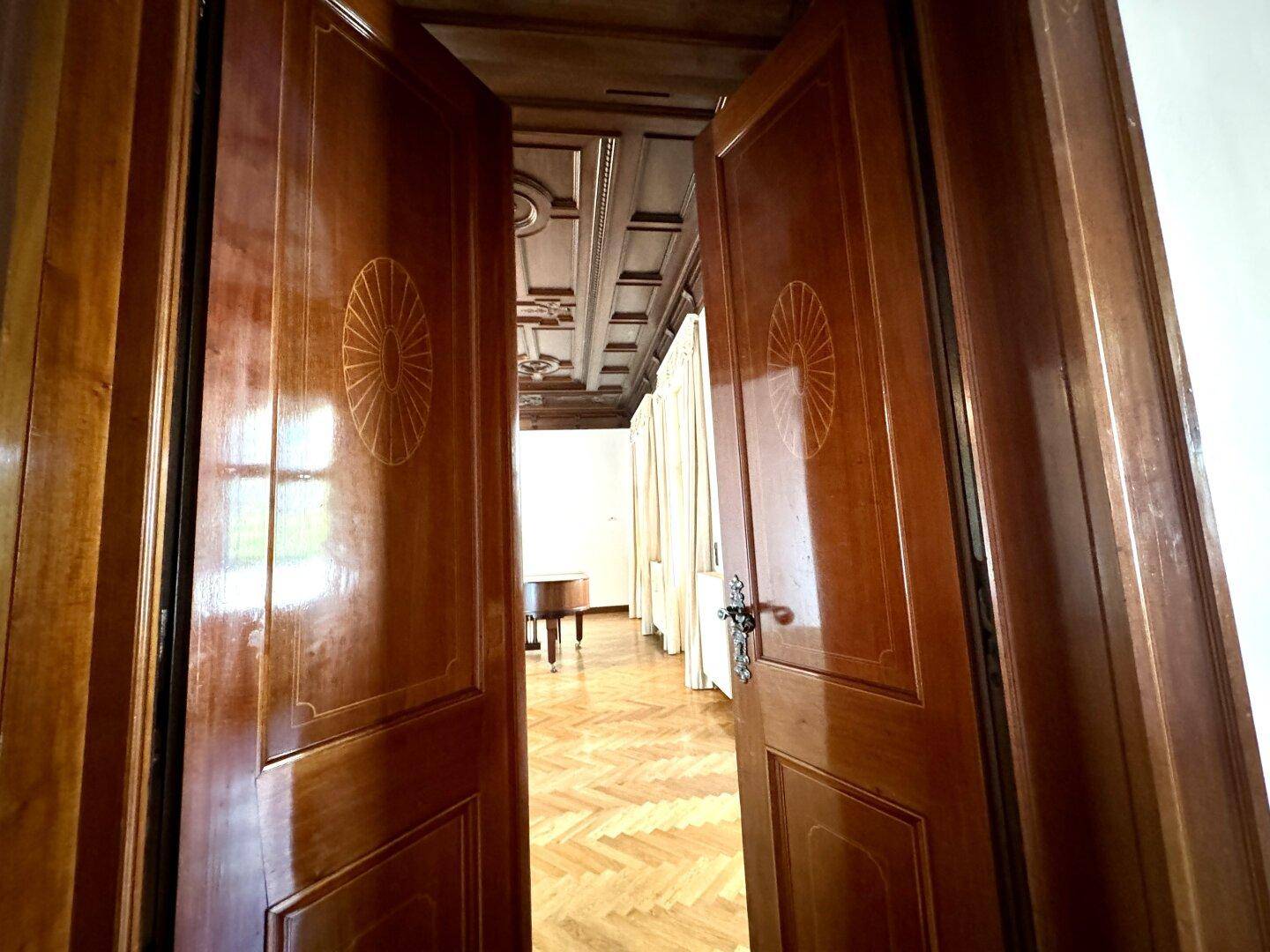 Elegante Doppeltüren aus Holz mit Intarsien, die in einen großzügigen Raum mit Parkettboden führen.