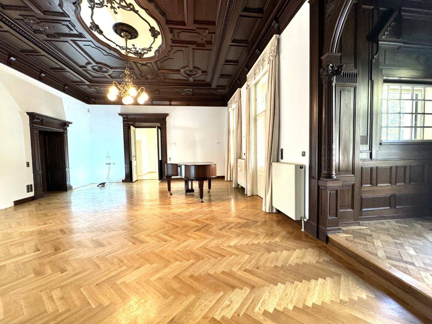 Großzügiger Wohnbereich mit historischer Kassettendecke, Parkettboden und viel Tageslicht, ideal für große Möbel.