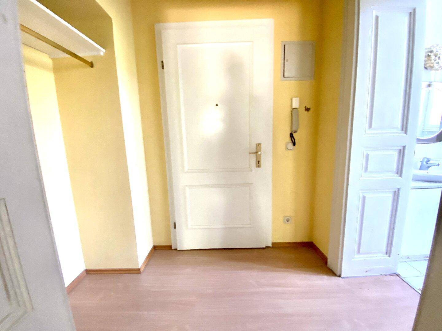 Eingangsbereich mit heller Wandfarbe, Holzboden und Gegensprechanlage, einladend gestaltet.