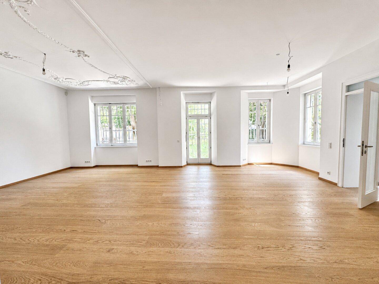 Geräumiges, leeres Wohnzimmer mit Eichenparkett und dekorativer Stuckdecke.