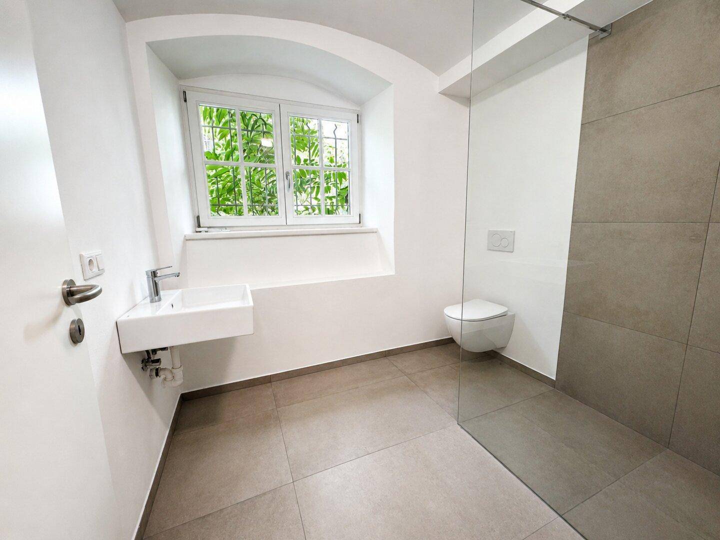Modernes Badezimmer im Keller mit Dusche, WC und Fenster.
