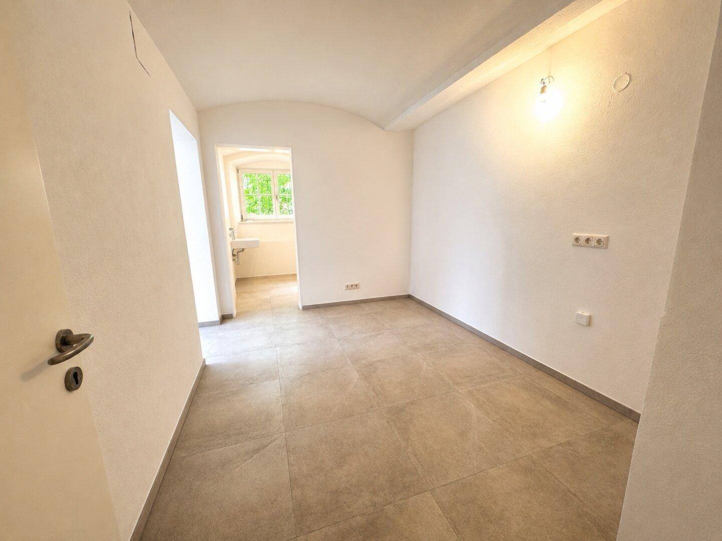Heller Kellerraum mit Fliesenboden und Zugang zu einem Badezimmer.