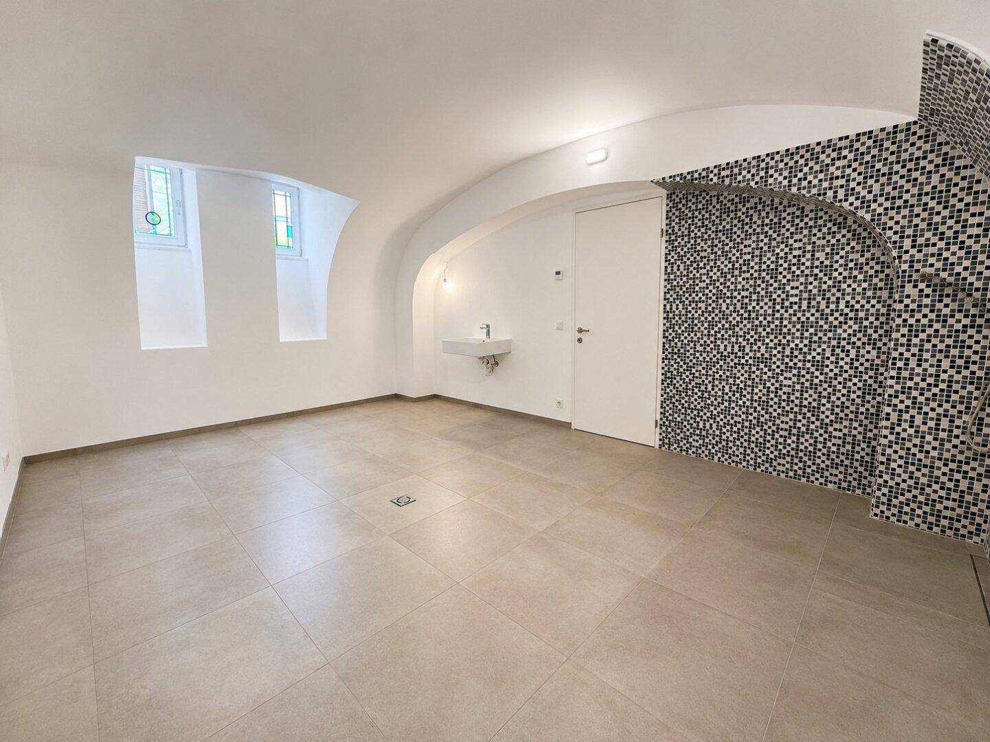 Renovierter Kellerraum mit Gewölbedecke, Fliesenboden und kleinem Waschbecken.