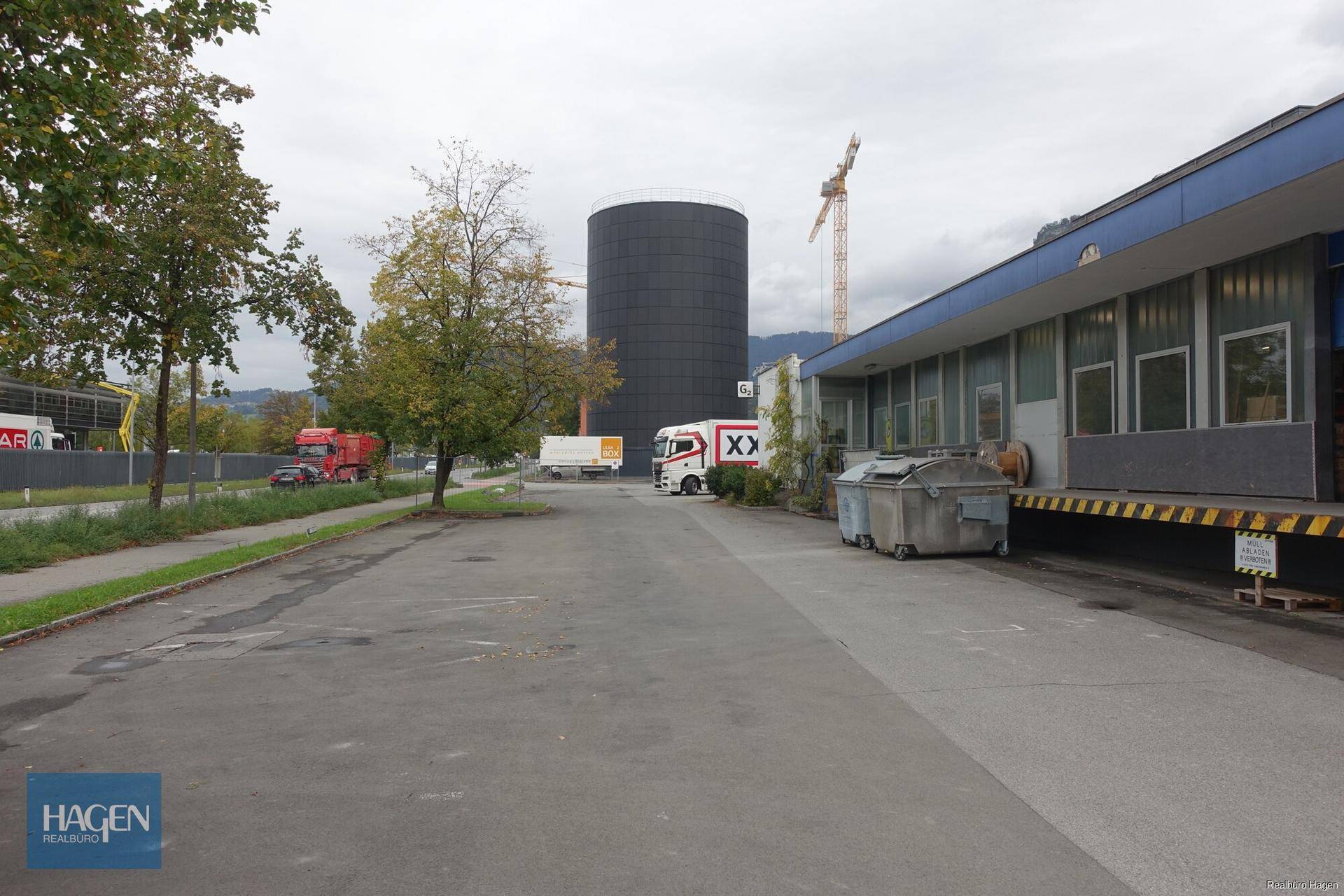 Außenansicht des Gebäudes mit Parkplatz, einem großen schwarzen Silo und einem Kran im Hintergrund.