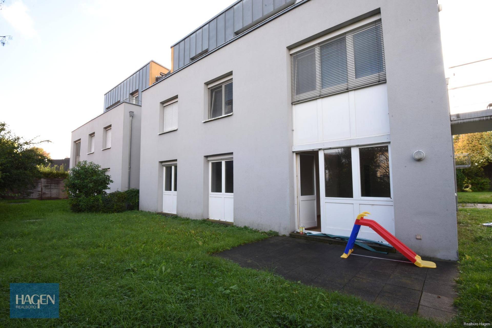 Rückansicht des Gebäudes mit Rasen und einer kleinen Kinderrutsche auf der Terrasse.