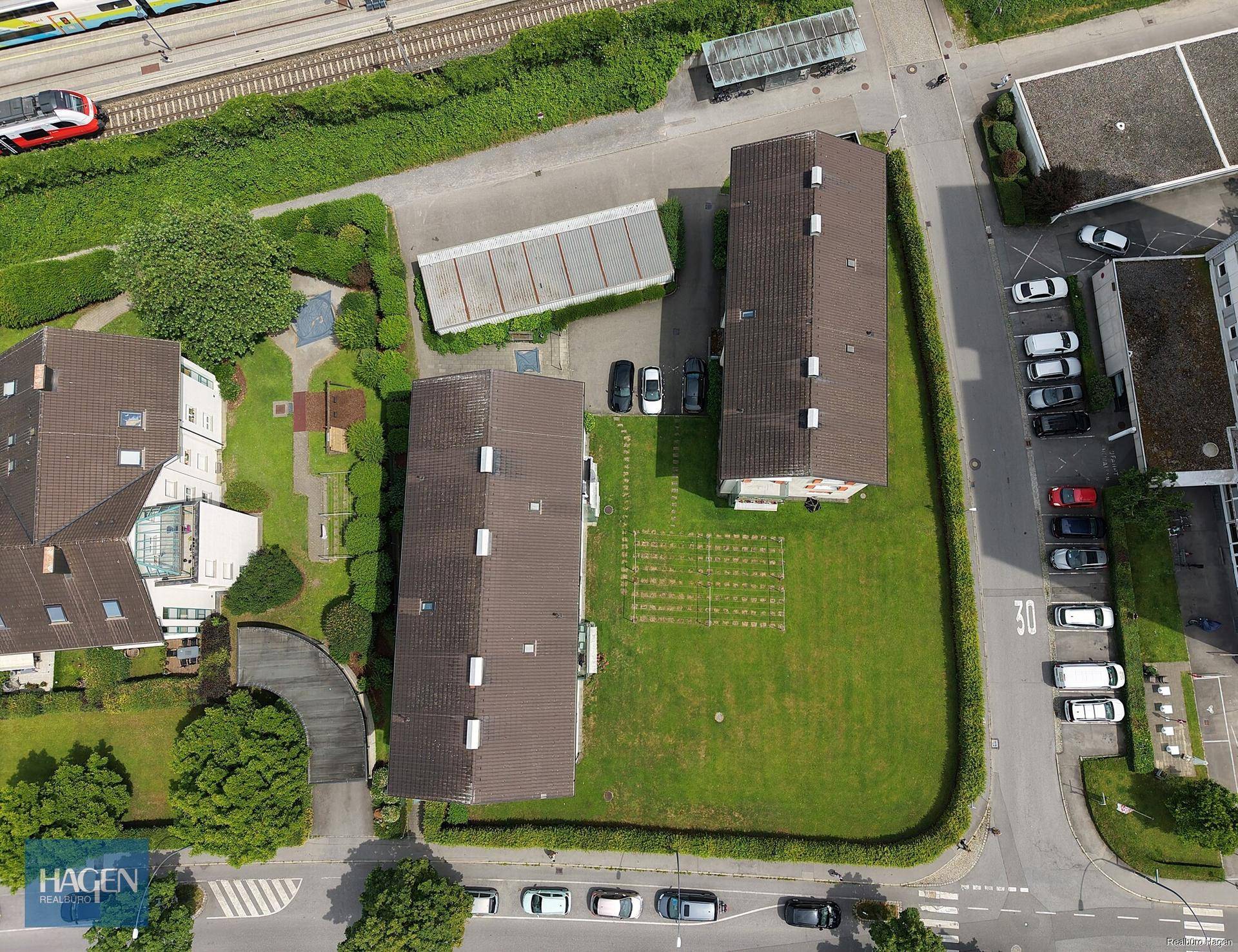 Vogelperspektive der Wohngebäude mit Parkplätzen und angrenzender Bahntrasse in einer städtischen Umgebung.