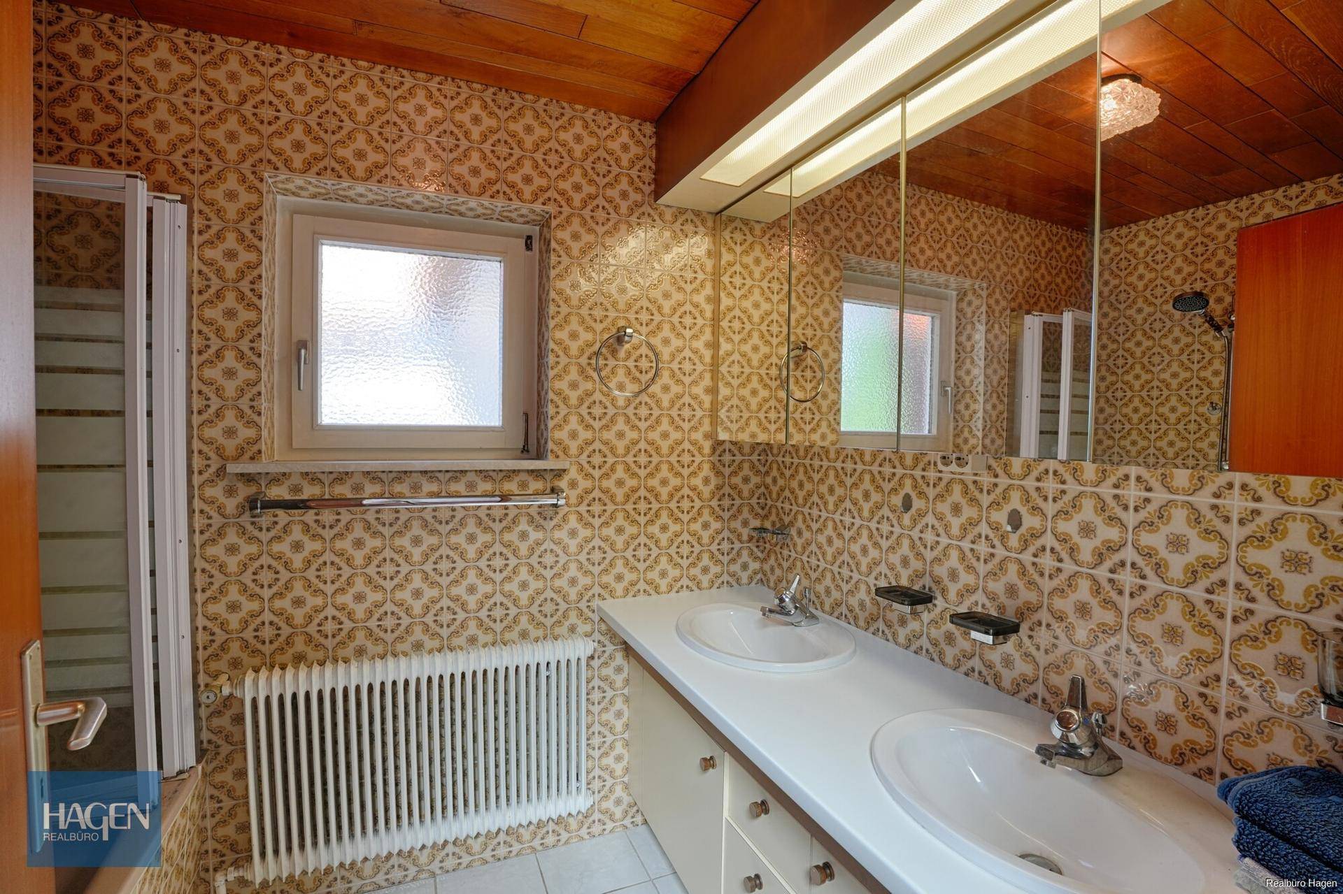 Badezimmer im 80er-Jahre-Stil mit gemusterten Fliesen, Doppelwaschbecken und Fenster.