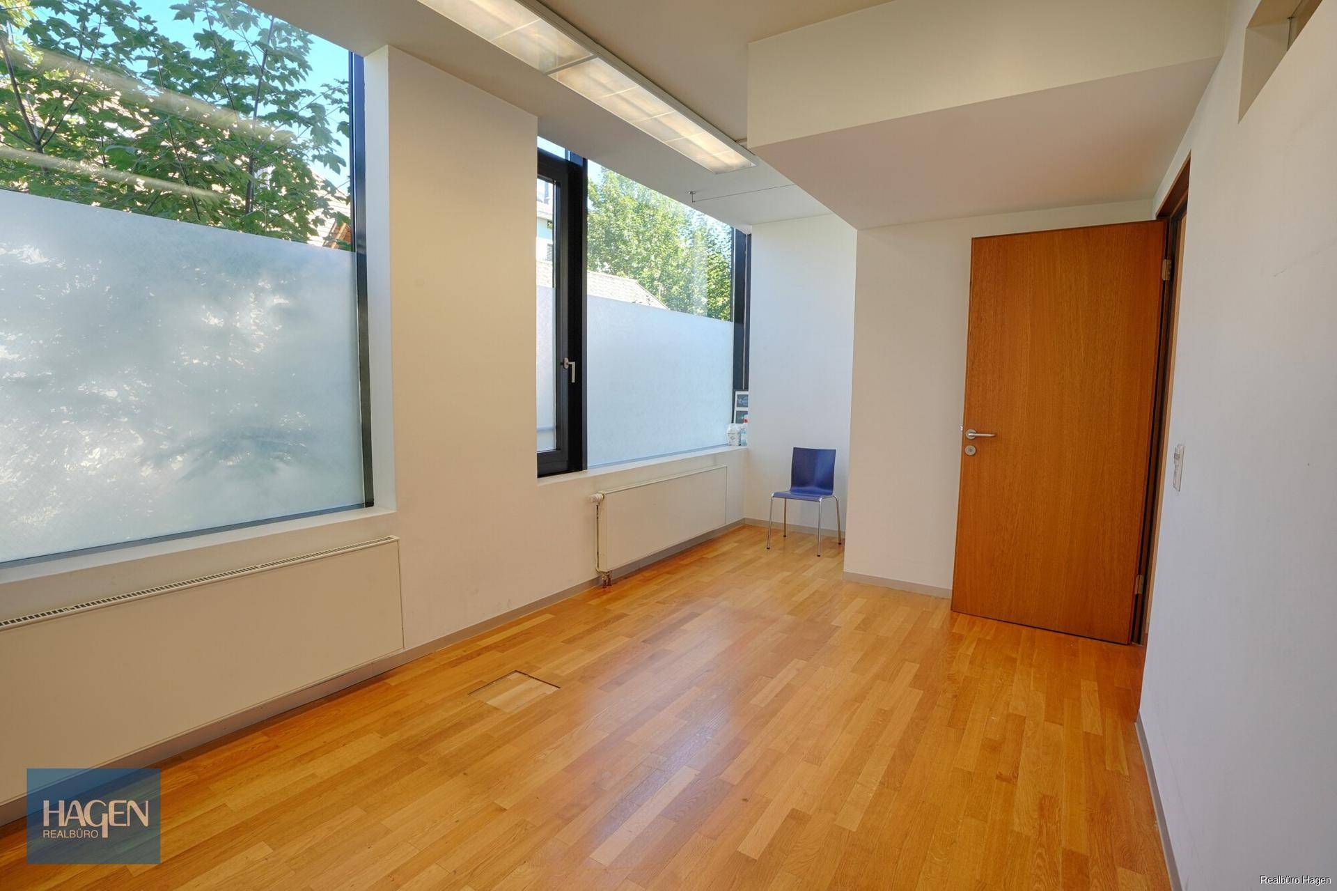 Leeres Büro mit großen Fenstern, die viel Tageslicht hereinlassen, und Holzfußboden.