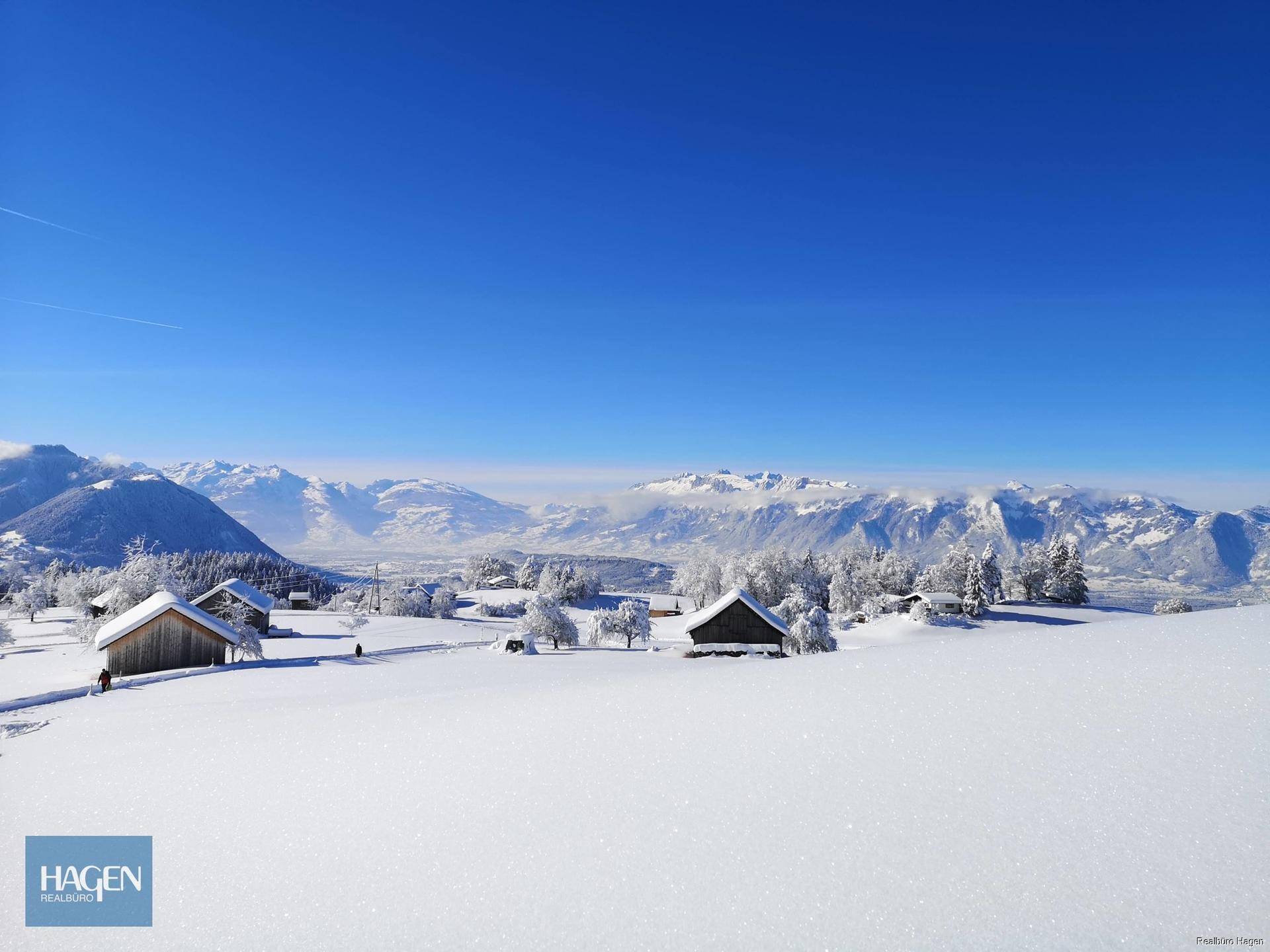 Weite, verschneite Winterlandschaft mit kleinen Häusern und majestätischen Bergen im Hintergrund.
